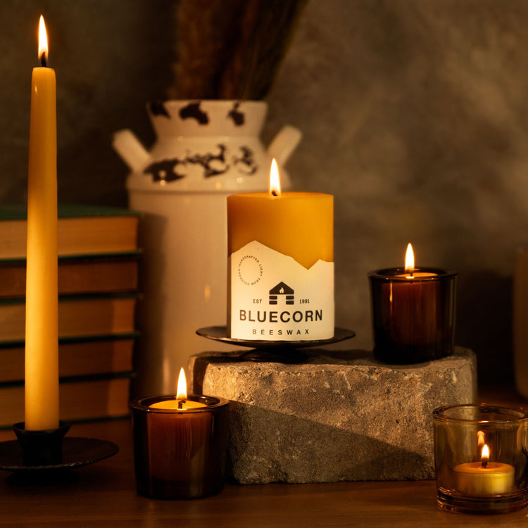 Bluecorn beeswax candles in their distinctive mountain range labels. These yellow, pure beeswax candles are lit and glowing.