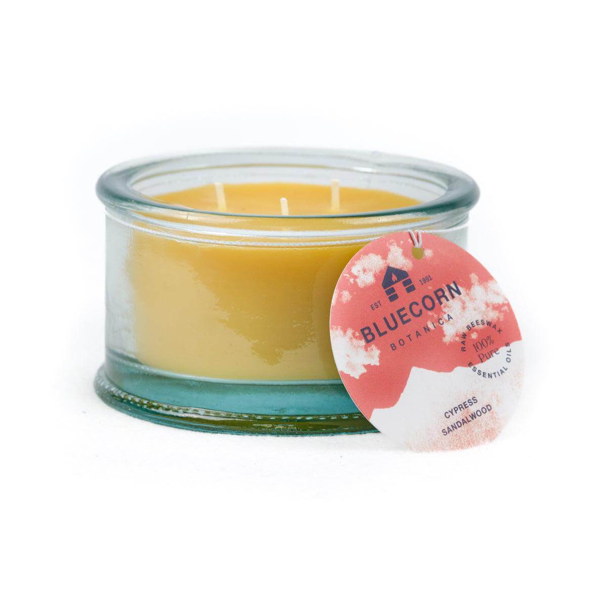 Bluecorn Botanica 100% Pure Beeswax Cypress and Sandalwood 10oz 3-Wick Glass Candle. Wax is golden in color and glass is clear colored, with a white back drop. Features red Bluecorn Botanica hang tag printed on 100% recyled paper with Bluecorn name and logo. Burn Time: 18 hours. Made with 100% Pure Beeswax, 100% Pure Essentail Oils and a 100% pure cotton wick, no lead. Candles are paraffin free, clean burning and non-toxic.