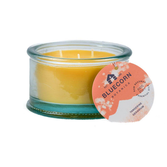 Bluecorn Botanica 100% Pure Beeswax Tangerine and Geranium 10oz 3-Wick Glass Candle. Wax is golden in color and glass is clear colored, with a white back drop. Features orange Bluecorn Botanica hang tag printed on 100% recyled paper with Bluecorn name and logo. Burn Time: 18 hours.  Made with 100% Pure Beeswax, 100% Pure Essentail Oils and a 100% pure cotton wick, no lead. Candles are paraffin free, clean burning and non-toxic.
