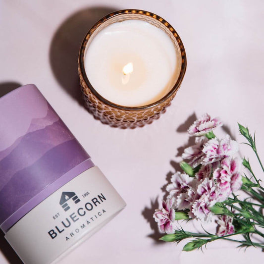 Scented candle in a decorative jar with a purple label and flowers nearby, creating a tranquil ambiance.