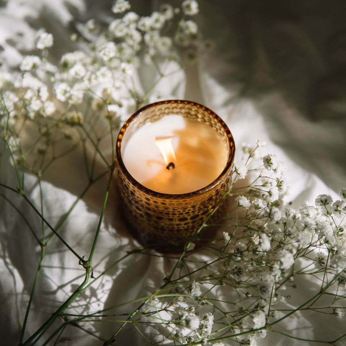 Scented jar candle surrounded by delicate white flowers, creating a serene and floral ambiance.