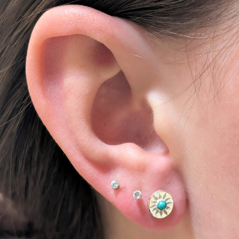 Close-up of an ear wearing three earrings with a focus on the turquoise stone earring.