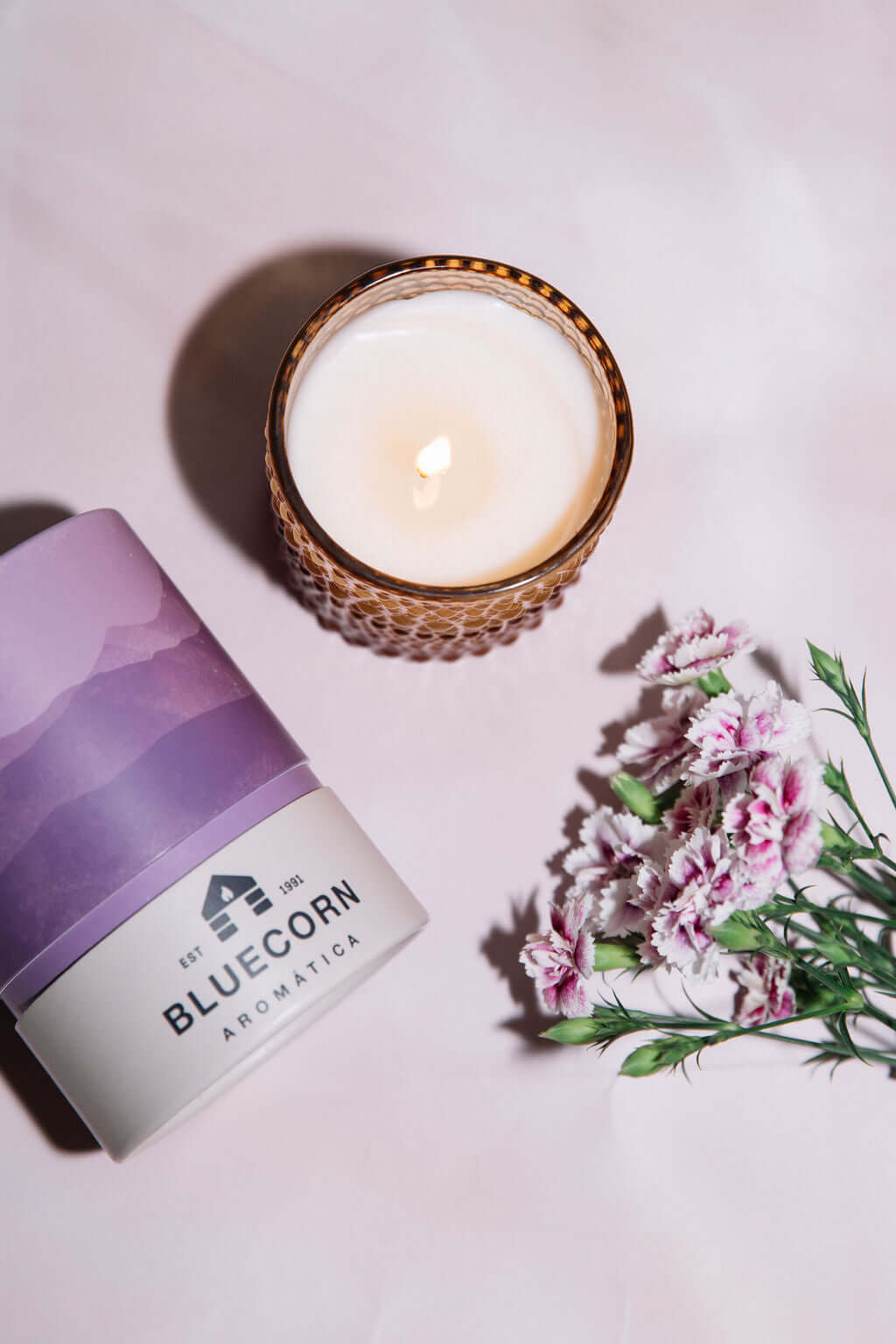 Candle in a beaded glass jar holder with a purple container labeled 'Bluecorn Aromatica' on a light background.