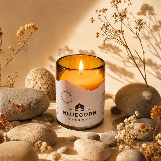 Bluecorn Beeswax candle in a glass container with stones and dried plants on a neutral background