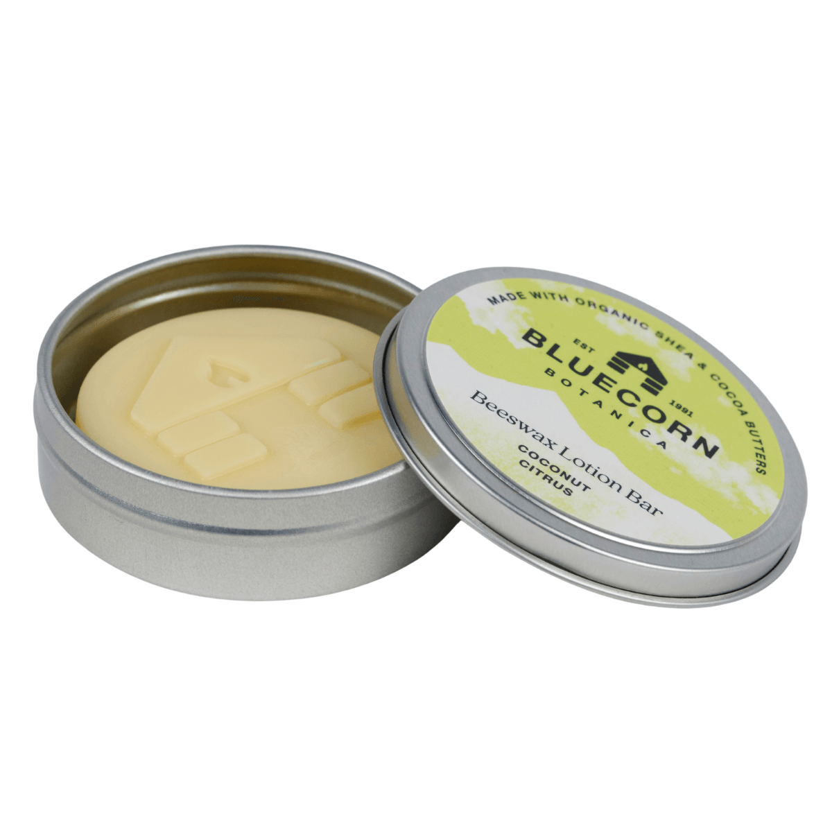 Bluecorn Botanica Beeswax Lotion Bar in Coconut Citrus. Made with Organic Shea Butter, Organic Cocoa Butter, Avocado Oil, Apricot Oil, Cappings Beeswax, Essential Oils. Using the warmth of your hands, these solids bars will turn into lotions. Can be used all over the body and come in a convenient tin. Features green Bluecorn Botanica Label on aluminum tin with opened lid showing lotion bar. Lotion bar is cream in color and features Bluecorn cabin.