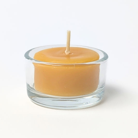 Beeswax tea light candle in a clear glass holder on a white background