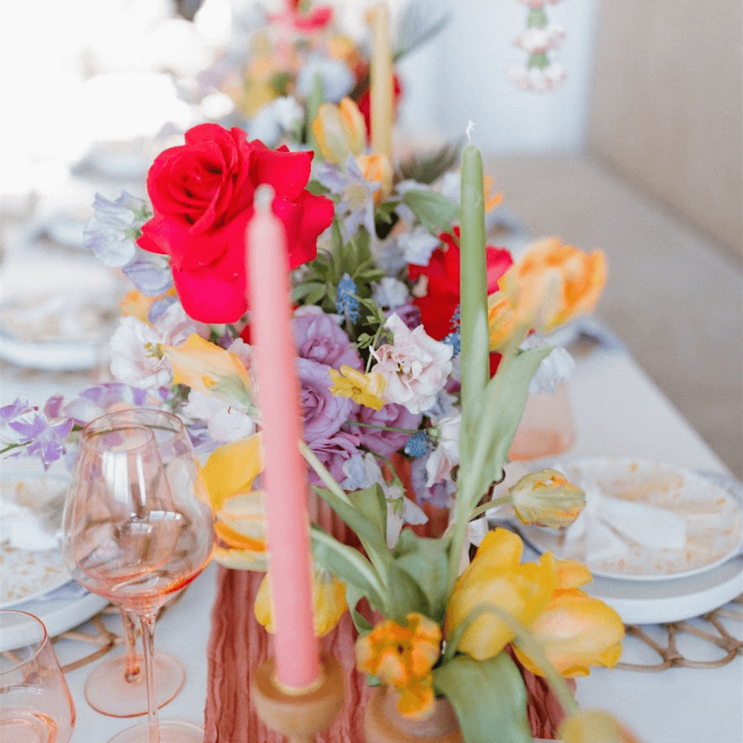 light pink taper candle from bluecorn candles in front of a floral spring table with green candlesticks