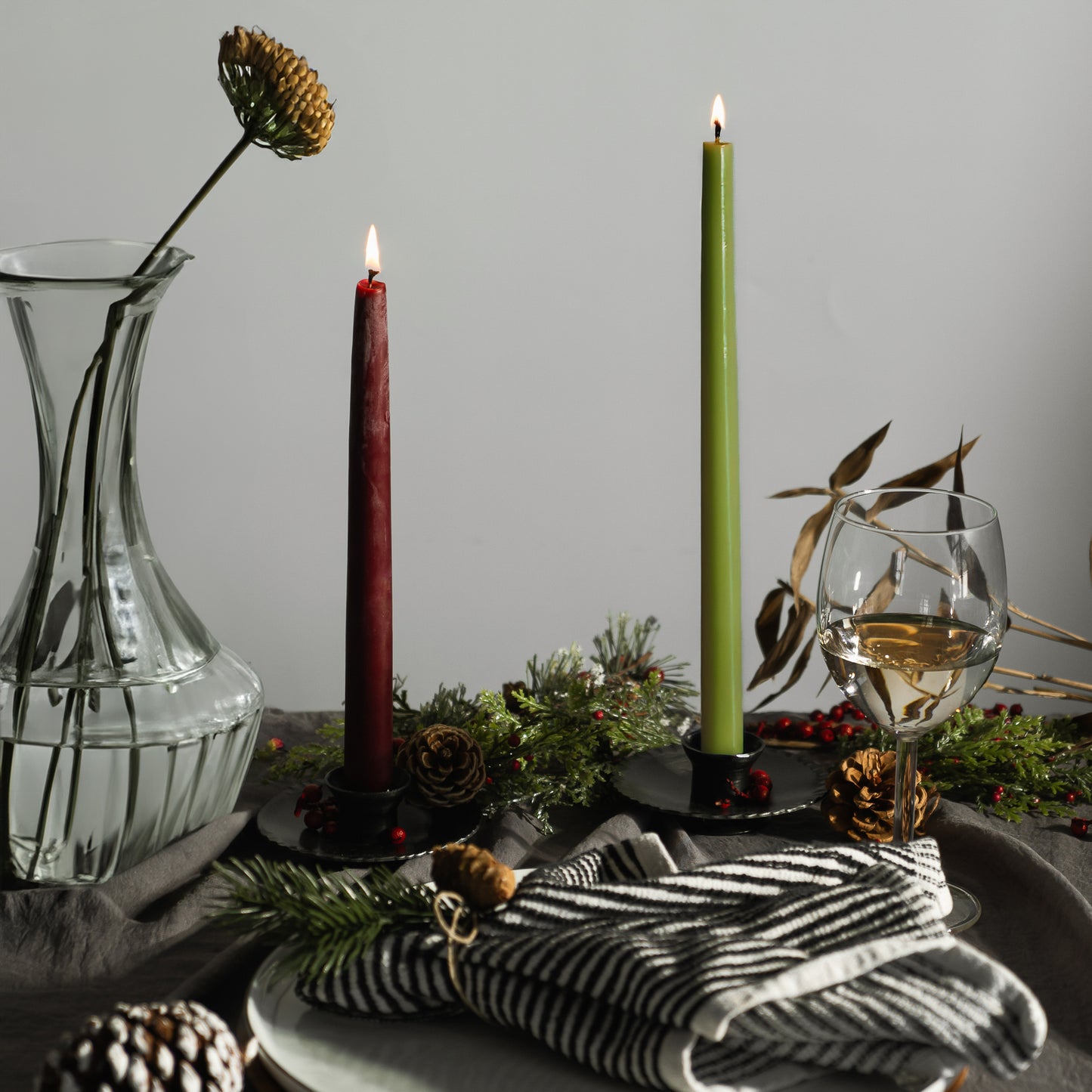 a dark red beeswax taper candle next to a light green beeswax taper candle for a modern holiday table