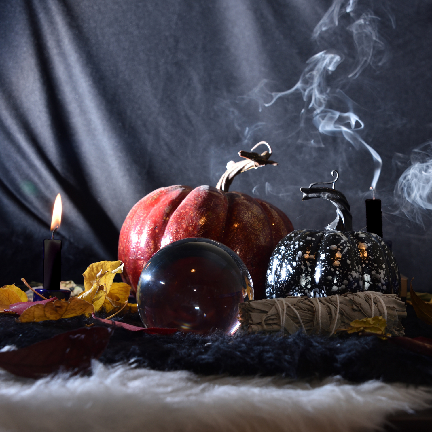 Black beeswax tapers beside a pumpkin, crystal ball and bundle of sage 