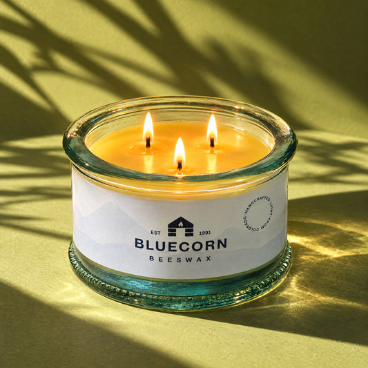 three wick beeswax candle with bluecorn beeswax logo lit and glowing on green background