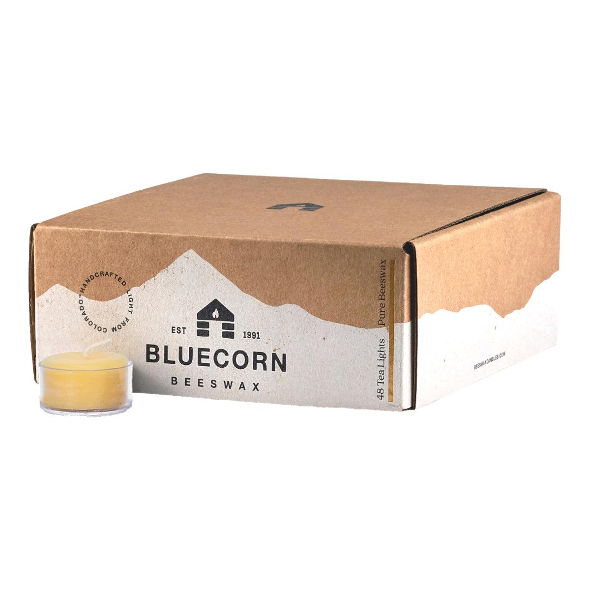 Bluecorn Beeswax 100% Pure Beeswax 48 Pack Raw Tea Light in Clear Cups. Picture features one Tea Light outside of Bluecorn branded Tea Light Box with a white background. Box features Bluecorn Beeswax name and logo, with an outline of Mt. Wilson in white printed on a 100% recycled kraft paper box. Tea lights will burn for about 5 hours each.
