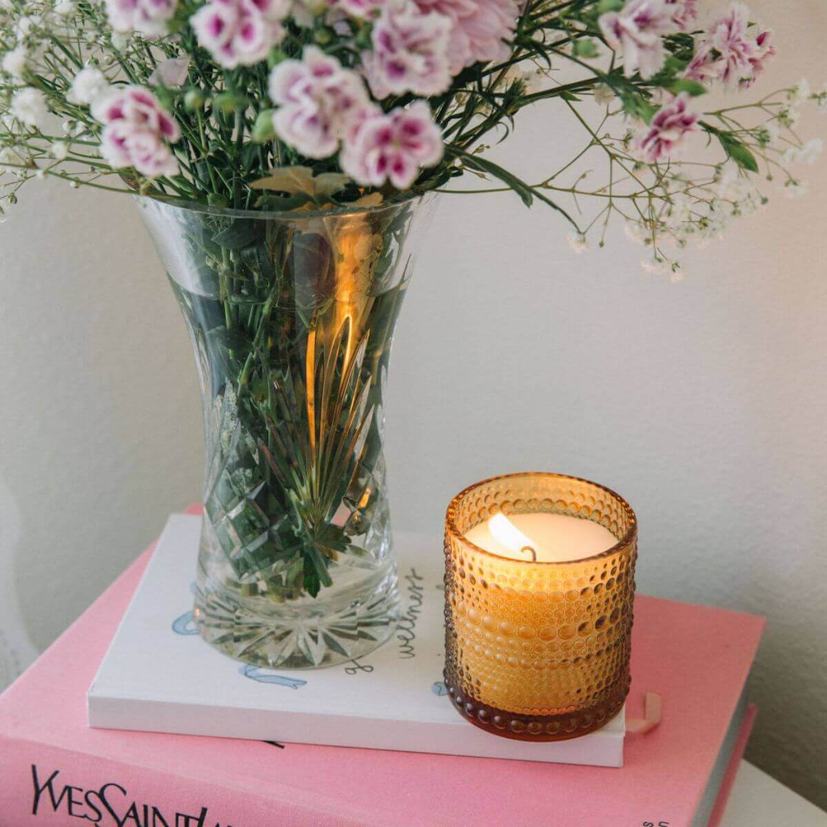 Vase with pink flowers and a lit candle on a pink surface
