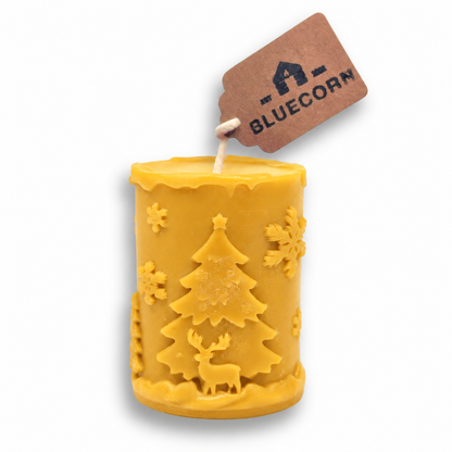 Raw golden beeswax Christmas pillar candle, unscented, with a raised winter scene of Christmas trees, reindeer and snowflakes.