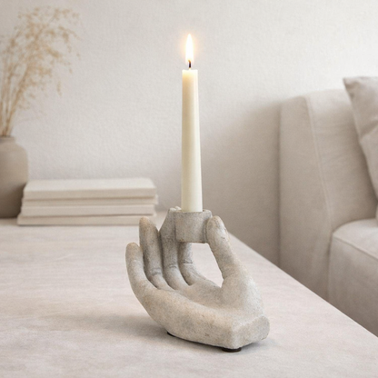 Candle holder shaped like a hand on a table with a candle, in a room setting.