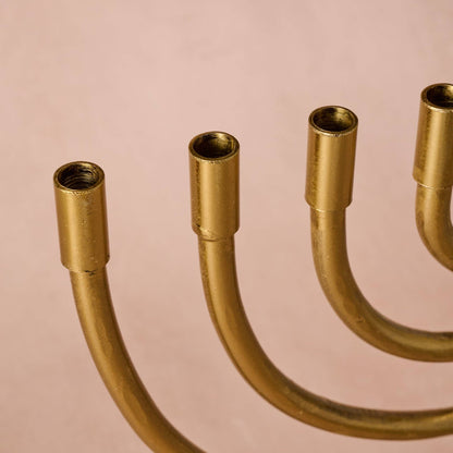 Close-up of a brass candelabra showing the five candle holders and curved arms against a solid pale pink background.
