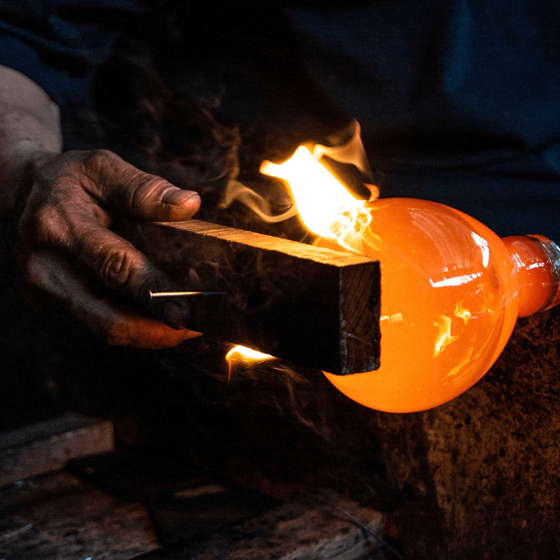 an artisan shapes the molten glass before creating a blown glass candle holder for bluecorn 
