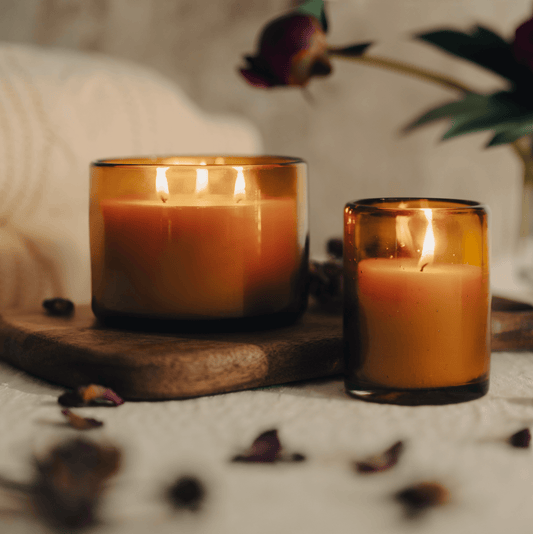 Beeswax jar candle and refill in blown glass holder, glowing with warm honeyed light on a wooden platter.