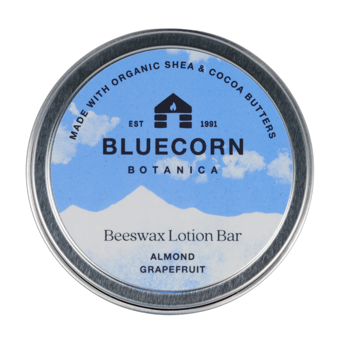 Bluecorn Botanica Beeswax Lotion Bar in Almond Grapefruit. Made with Organic Shea Butter, Organic Cocoa Butter, Avocado Oil, Apricot Oil, Cappings Beeswax, Essential Oils. Using the warmth of your hands, these solids bars will turn into lotions. Can be used all over the body and come in a convenient tin. Features blue Bluecorn Botanica Label on aluminum tin with opened lid showing lotion bar. Lotion bar is cream in color and features Bluecorn cabin.