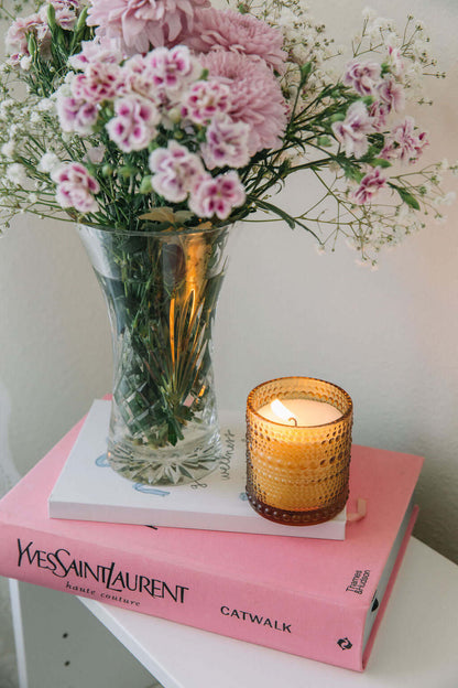 Pink flowers in a vase on a pink book with a lit scented candle from bluecorn