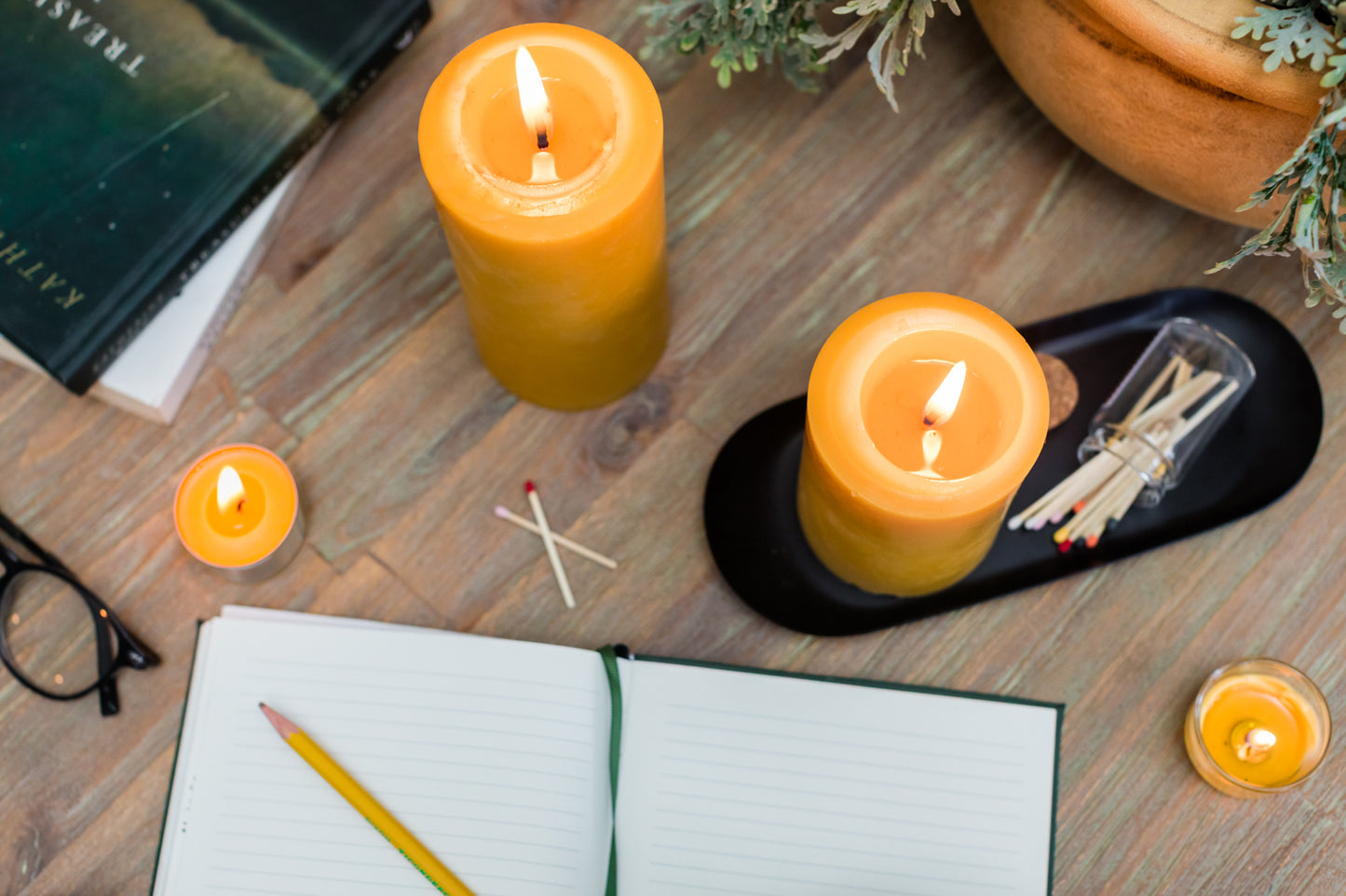 Candles on a wooden surface with matches and a notebook.
