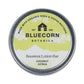 Bluecorn Botanica Beeswax Lotion Bar in Coconut Citrus. Made with Organic Shea Butter, Organic Cocoa Butter, Avocado Oil, Apricot Oil, Cappings Beeswax, Essential Oils. Using the warmth of your hands, these solids bars will turn into lotions. Can be used all over the body and come in a convenient tin. Features green Bluecorn Botanica Label on aluminum tin with opened lid showing lotion bar. Lotion bar is cream in color and features Bluecorn cabin.