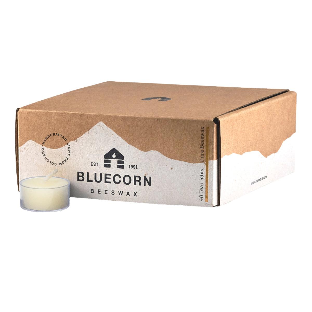 Bluecorn Beeswax 100% Pure Beeswax 48 Pack Ivory Tea Light in Clear cups. Picture features one Tea Light outside of Bluecorn branded Tea Light Box with a white background. Box features Bluecorn Beeswax name and logo, with an outline of Mt. Wilson in white printed on a 100% recycled kraft paper box. Tea lights will burn for about 5 hours each.
