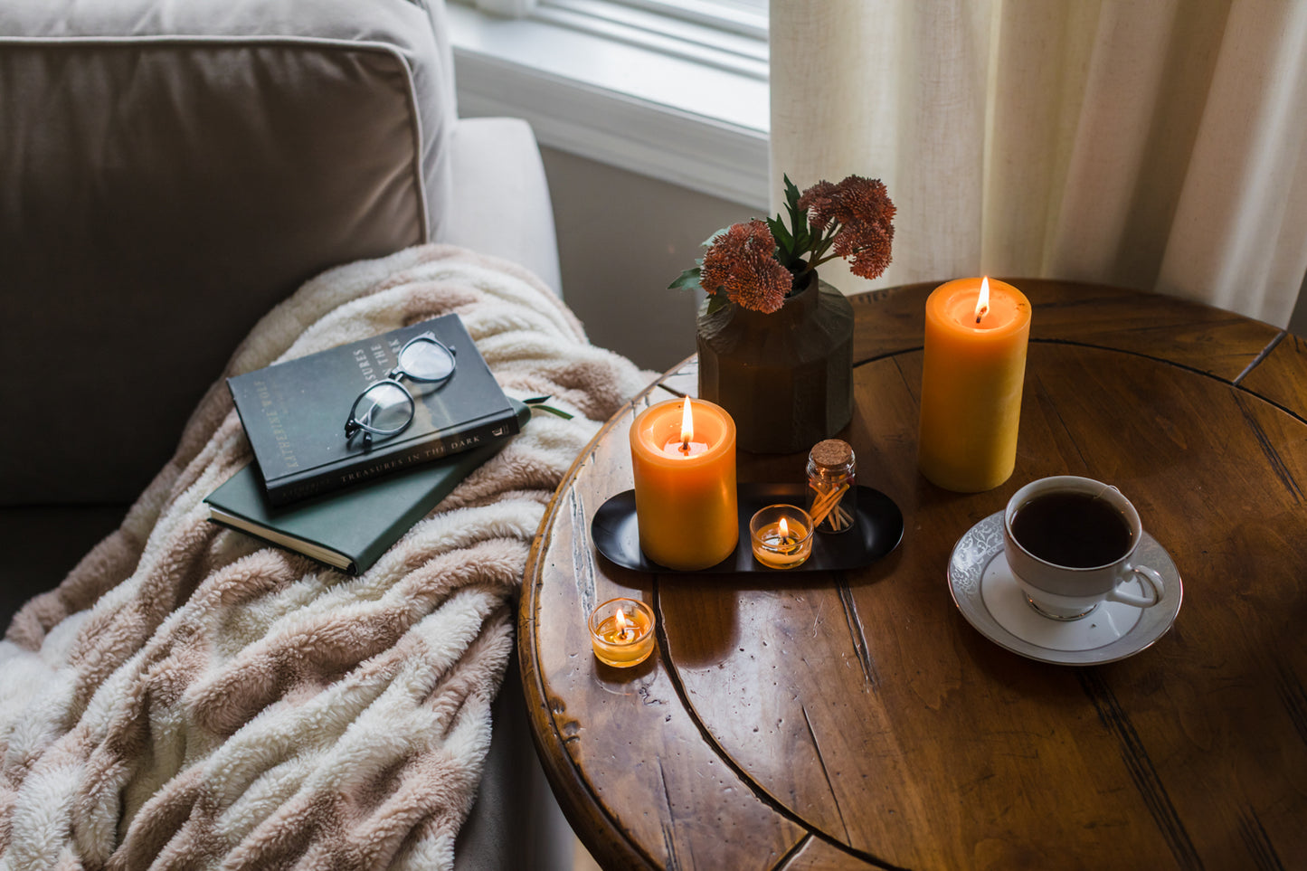 Candlelit scene with a book, glasses, flowers, and coffee on a wooden table.