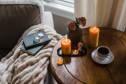 Candlelit scene with a book, glasses, flowers, and coffee on a wooden table.