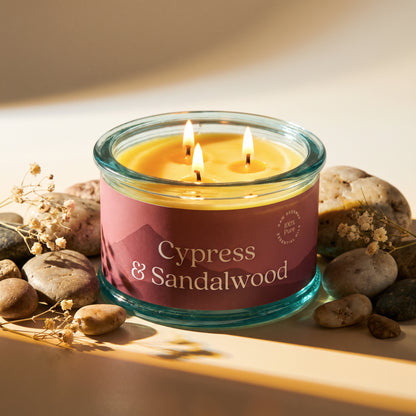 cypress and sandalwood scented beeswax candle with three wicks lit and glowing surrounded by stones 