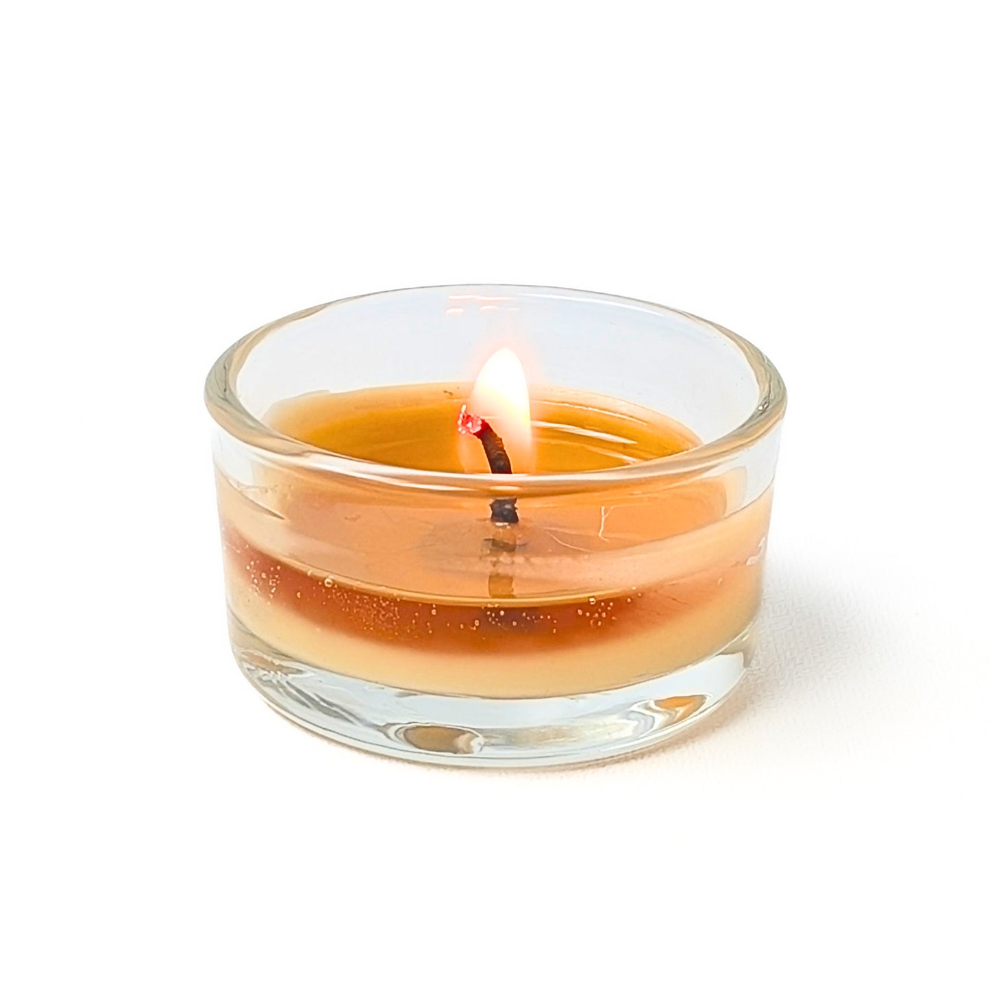 beeswax tea candle with a lit wick in a refillable glass tea light holder on a white background