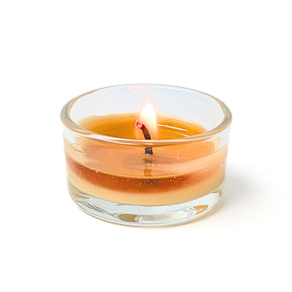 beeswax tea candle with a lit wick in a refillable glass tea light holder on a white background