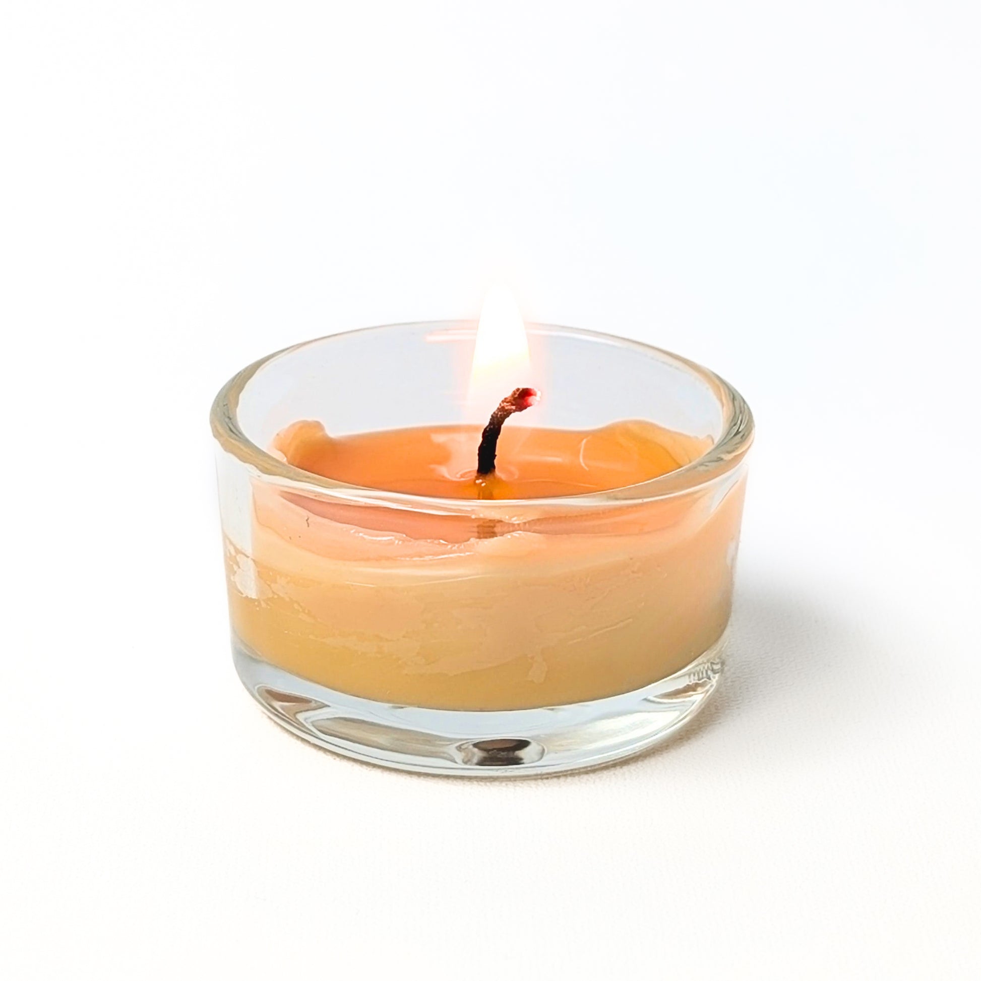 Small glass candle with a lit wick on a white background