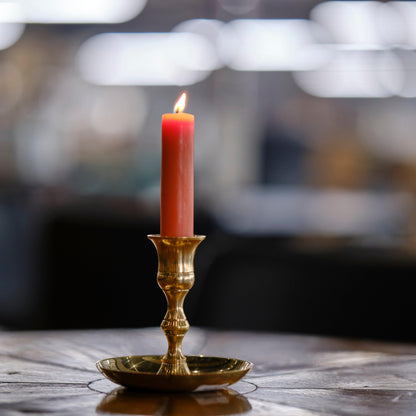 A pink candlestick made of pure beeswax burns in a brass taper candle holder at Bluecorn Candle's workshop in Colorado