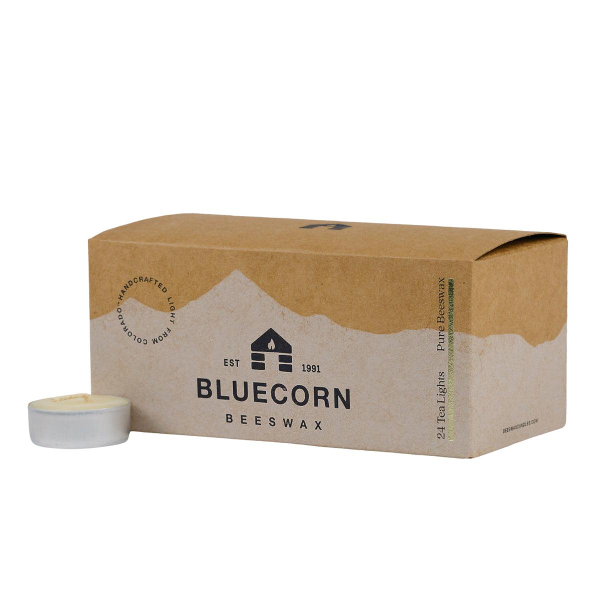 Bluecorn Beeswax 100% Pure Beeswax 24 Pack Ivory Tea Light in Metal cups. Picture features one Tea Light outside of Bluecorn branded Tea Light Box with a white background. Box features Bluecorn Beeswax name and logo, with an outline of Mt. Wilson in white printed on a 100% recycled kraft paper box. Tea lights will burn for about 5 hours each.