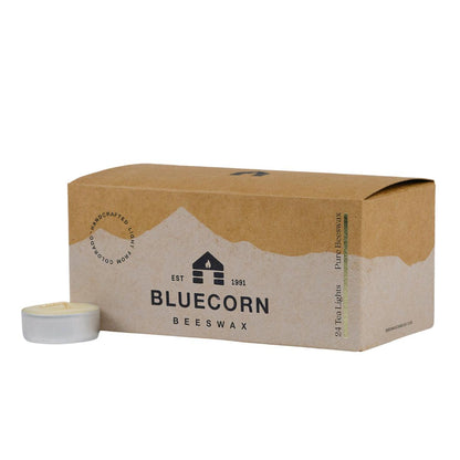 Bluecorn Beeswax 100% Pure Beeswax 24 Pack Ivory Tea Light in Metal cups. Picture features one Tea Light outside of Bluecorn branded Tea Light Box with a white background. Box features Bluecorn Beeswax name and logo, with an outline of Mt. Wilson in white printed on a 100% recycled kraft paper box. Tea lights will burn for about 5 hours each.