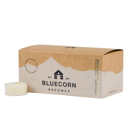 Bluecorn Beeswax 100% Pure Beeswax 24 Pack Ivory Tea Light in Clear cups. Picture features one Tea Light outside of Bluecorn branded Tea Light Box with a white background. Box features Bluecorn Beeswax name and logo, with an outline of Mt. Wilson in white printed on a 100% recycled kraft paper box. Tea lights will burn for about 5 hours each.