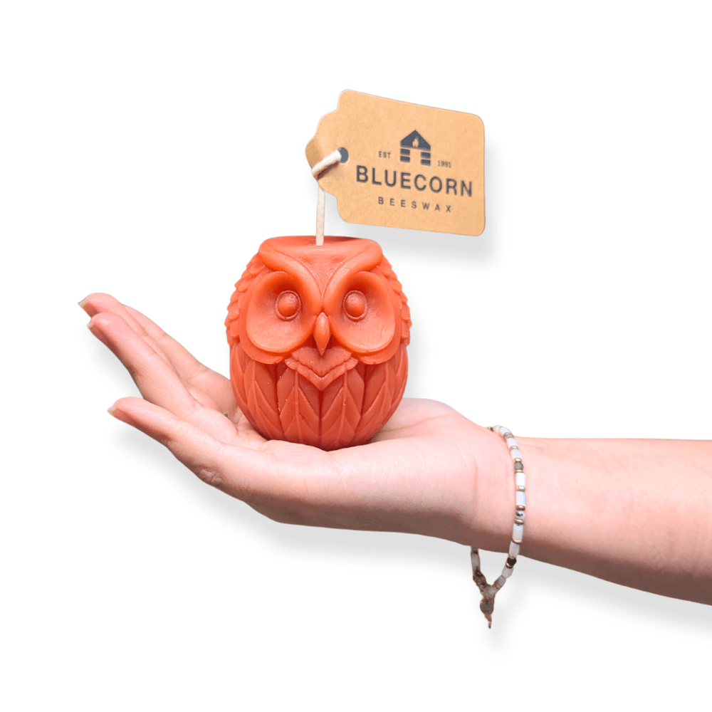 Orange owl shaped beeswax candle held in a hand, showing its 3 inch scale and whimsical sculpted detail.