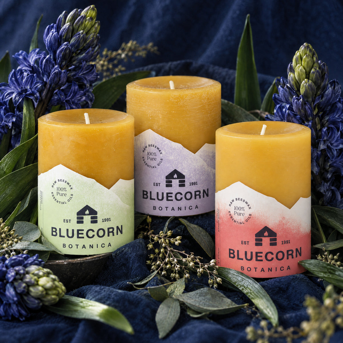 bluecorn botanica scented beeswax pillar spring trio on blue velvet background with purple flowers