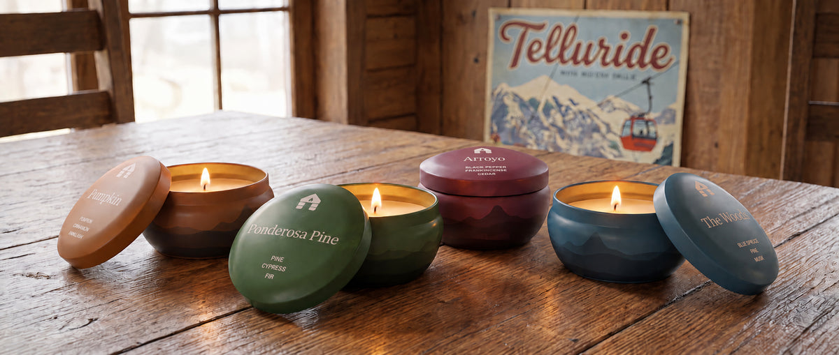 pumpkin spice scented candle tin with pine, arroyo and the woodsy winter scented candles made in colorado by bluecorn with telluride poster in background