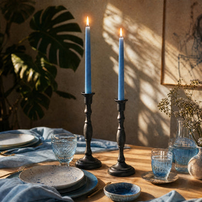 Dining table setting with light blue beeswax taper candles, plates, and glasses on a wooden table.