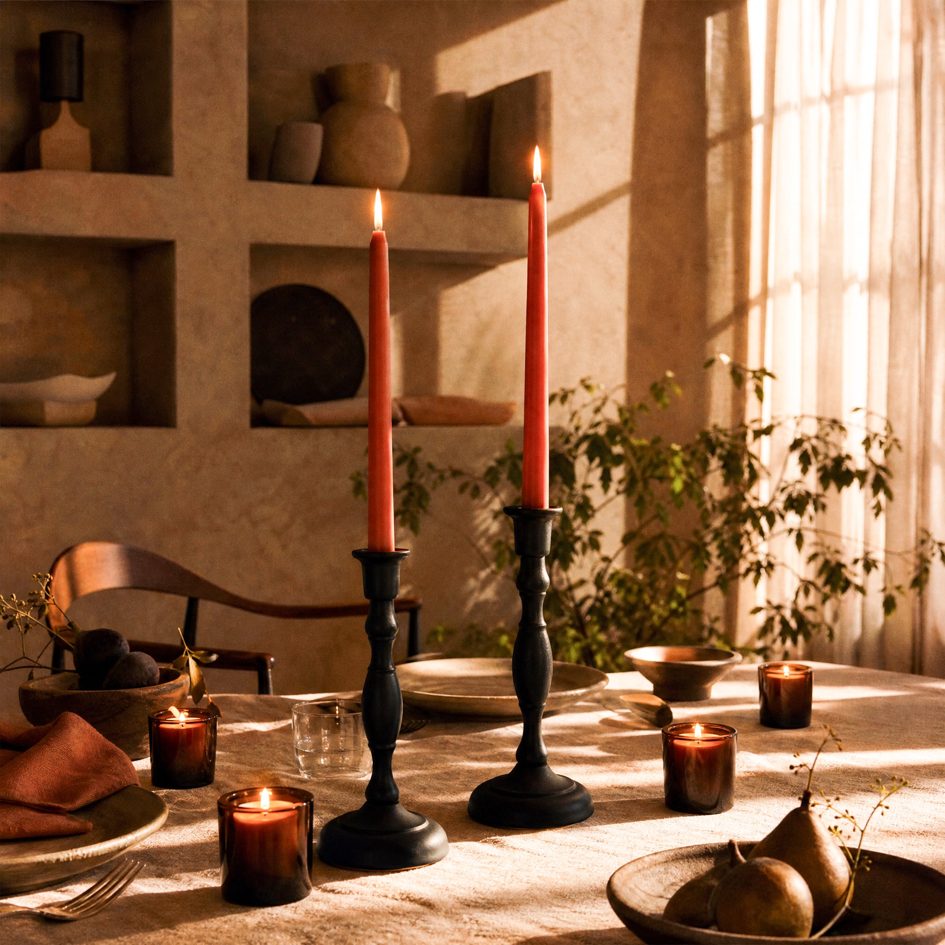 Dining table set with terracotta tapered candles and plates in a warm, softly lit room. Bluecorn beeswax votives in amber glass holders scattered around